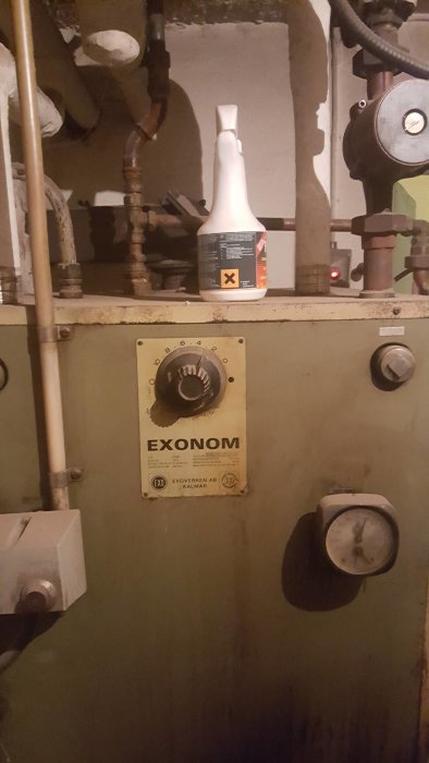 Gammal värmepanna med reglage märkt EXONOM, rör och ventilationskanaler, samt rengöringsmedel på toppen.