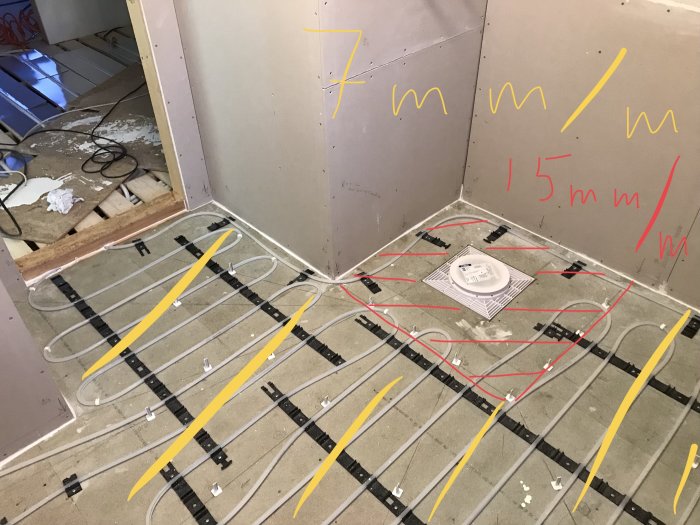 Installation av vattenburen golvvärme över golvspån med måttmarkeringar och avloppsbrunn i pågående badrumsrenovering.