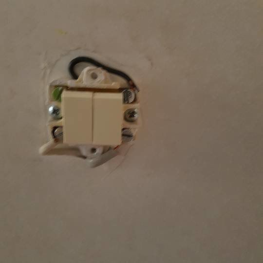 Öppen elektrisk kronbrytare i vägg med tre synliga trådar och en vit knapp.