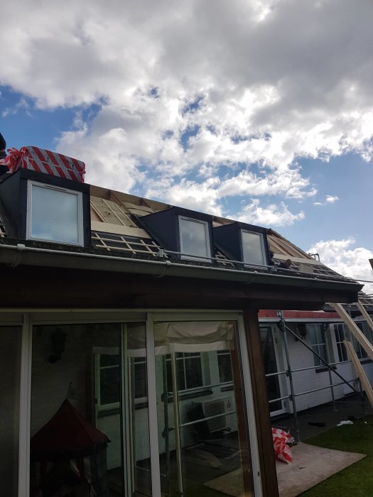 Hus med ombyggt tak och fönsterkupor under arbete, med byggnadsställning och presenning.