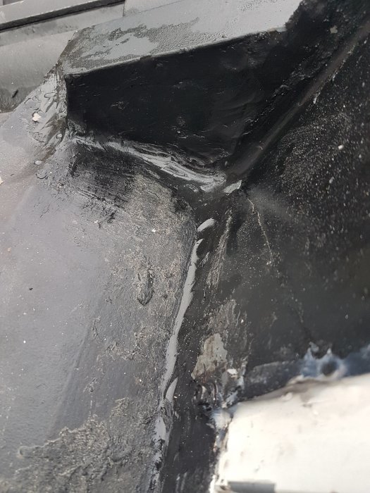 Närbild av ett tak med ny och gammal papp där den gamla pappen är blöt och nya pappen är vikt åt sidan.