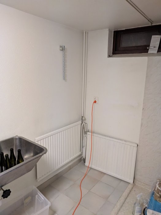 Värmeelement i källare med synliga rör och elkabel, planerad att flyttas för grovköksinstallation.
