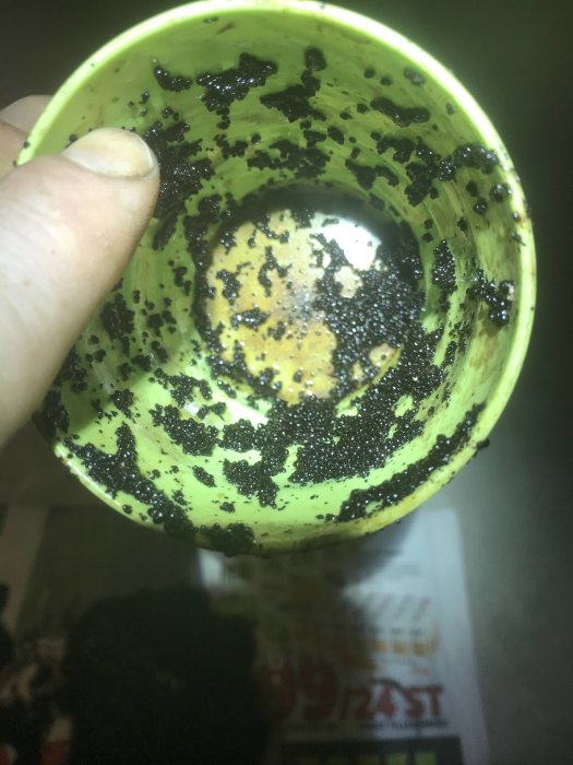 Hand håller en grön ejektor med små svarta korn av filtermassa som täcker ytan.