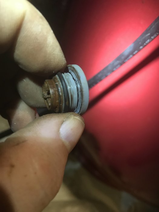 Hand som håller en skadad och rostig vattenplugg framför en röd rörledning.
