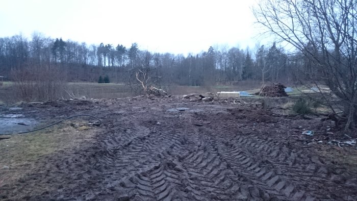 Renoverad stallplats med bortschaktade stenar och däckspår i lerig mark, med skymning som bakgrund.