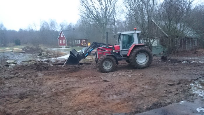 Traktor med frontlastare schaktar bort sten och jord vid rivningsarbete av stall.