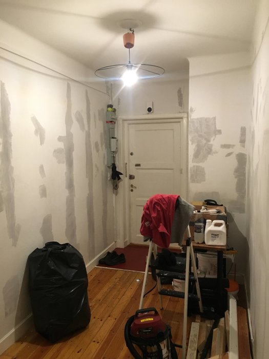 Hall under renovering med punktspacklade väggar, verktyg och byggmaterial på golvet.