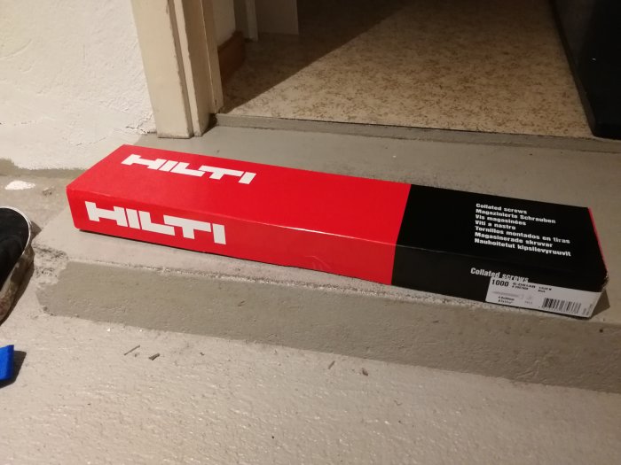 En låda med Hilti-kolladskruvar för byggprojekt placerad på ett betonggolv.