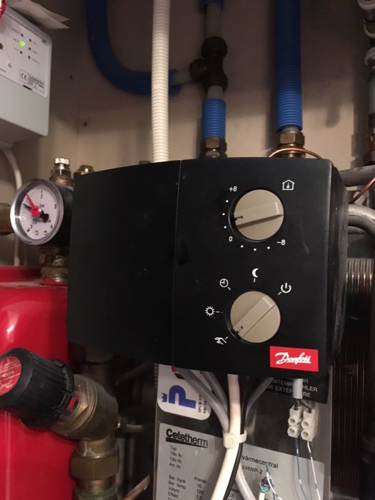 Analog Danfoss regulator inställd på manuellt läge, monterad vid värmesystem med synliga rör och mätare.