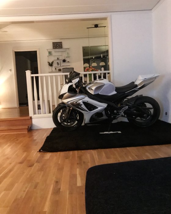 Motorcykel parkerad inomhus på en svart matta i ett vardagsrum.