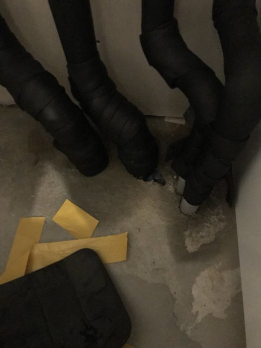 Blöta betongplattor och isolerade rörledningar med synlig fukt och rörgenomföringar.