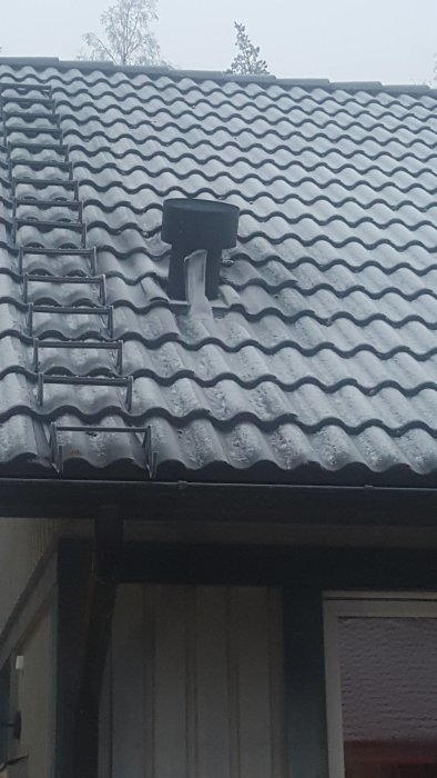 Takventil med stor istapp i vintertid på ett snötäckt hustak.