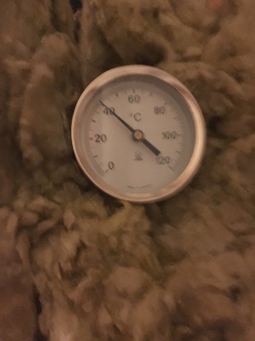 Termometer som visar ungefär 60 grader Celsius, oskarp bakgrund med isoleringsmaterial.