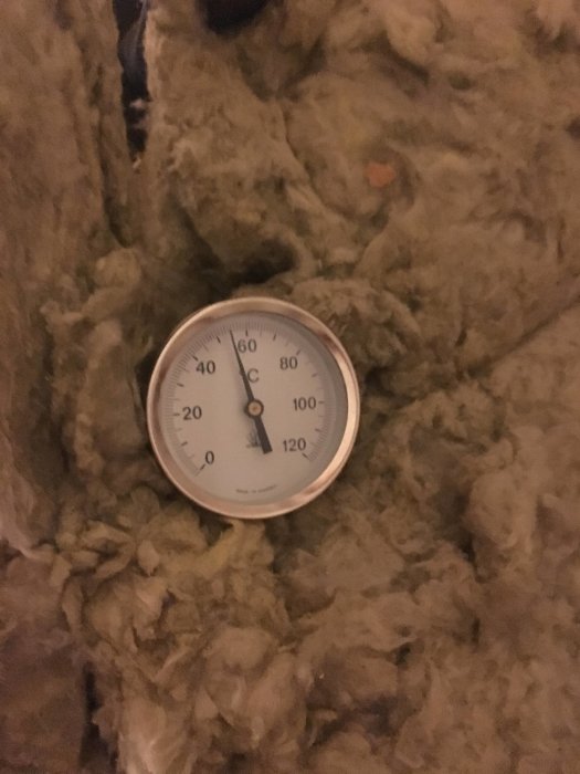 Analoga termometern visar cirka 75 grader Celsius, monterad på en ackumulatortank omgiven av isolering.