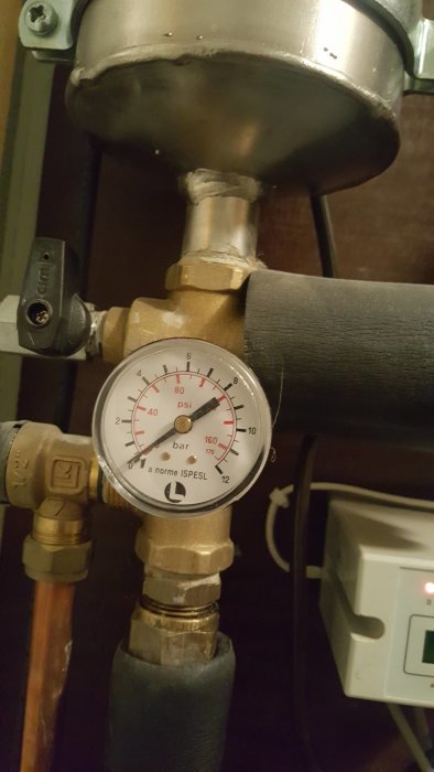 Manometer med lågt tryckvisning i en uppvärmningsanläggning med svarta och kopparledningar.