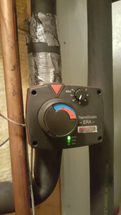 Reglagenhet för värmesystem med mätare och knappar på en vägg, bredvid isolerade rör.