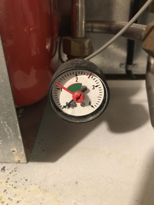 Manometer med röd visare som står på 1 bar, monterad på rörledning, i teknisk miljö.