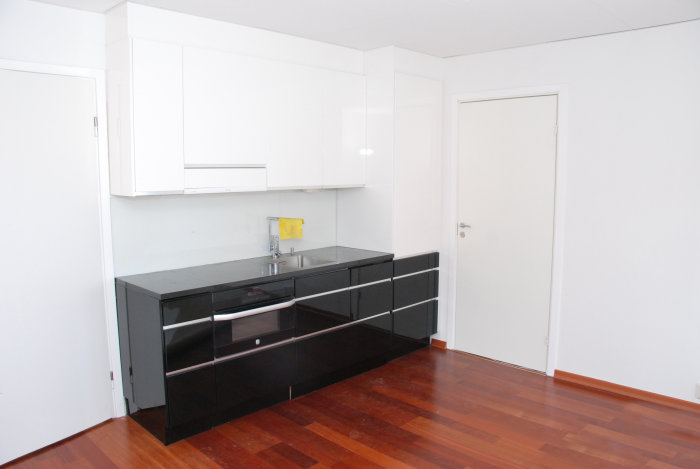 Modernt kök med vita skåp och svart bänkskiva, inklusive en integrerad 40 cm bred diskmaskin.