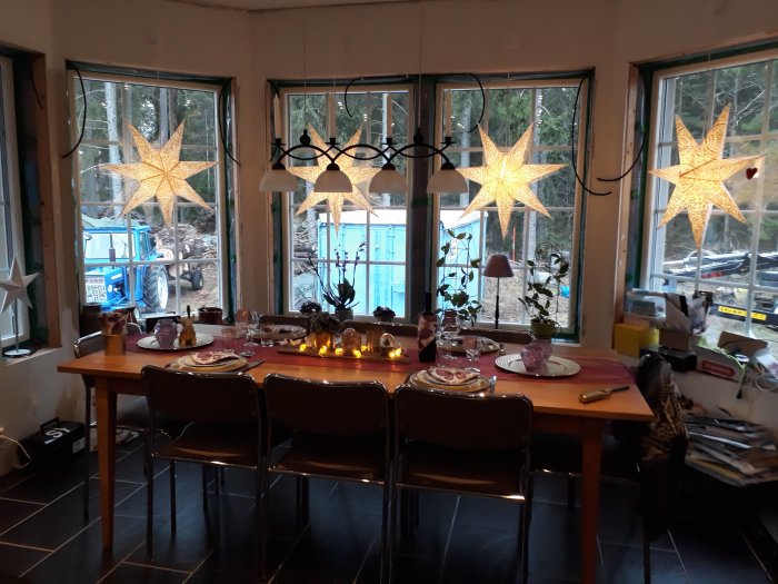 Ett middagsbord dukat för fest med belysning och stjärnformade fönsterlampor i ett hemtrevligt rum.