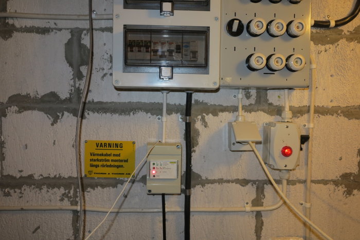 Elcentral med varningskylt och justerad apparat indikerande påslagen värmekabel via röd diod.