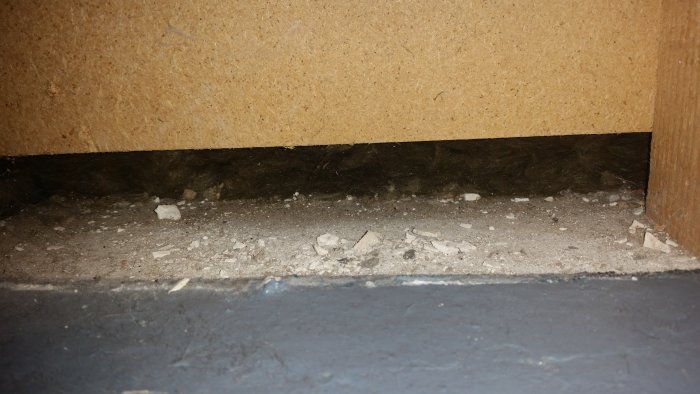 Öppen vägg avslöjar en gammal fuktskada med murbruk och skräp vid husgrunden, tecken på möjligt mögelproblem.