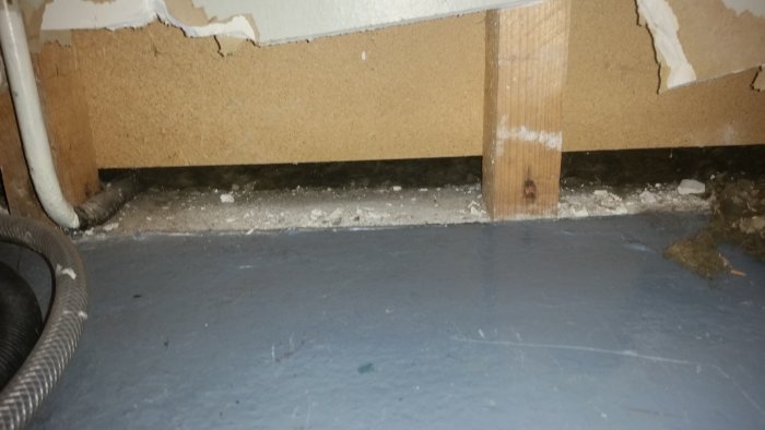 Vägg med upptornat gips och synlig skada längst ner, indikerar fuktskada i byggnad.