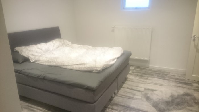 Nyrenoverat sovrum i källare med säng, ljust golv, matta och radiator.