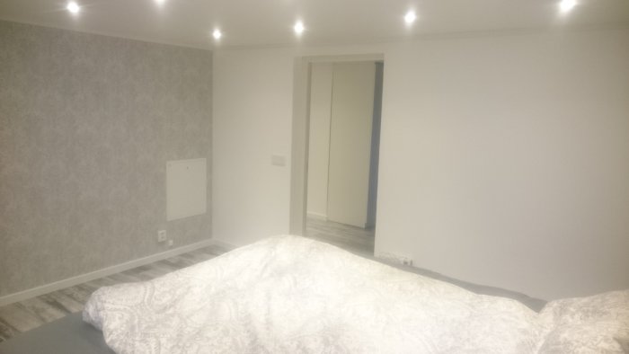 Renoverat sovrum med tapetserade väggar, infällda taklampor och garderob.