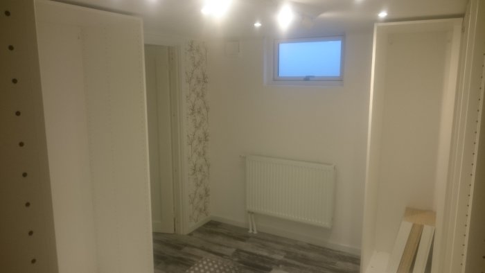 Nyrenoverad källarkorridor med inbyggda garderober, radiator och träfärgat golv.