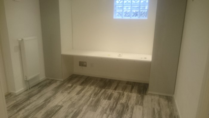 Renoverat rum i källare med laminatgolv och lång vit bänkskiva under fönster.