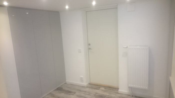 Nyrenoverad källarkorridor med garderob, vit dörr och en radiator.