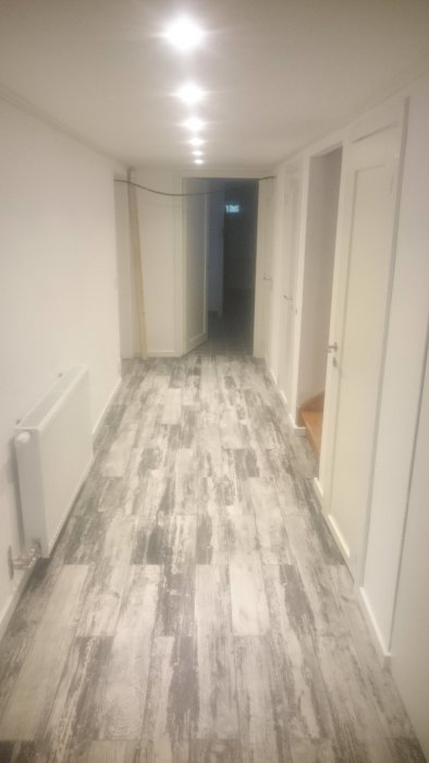 Nyrenoverad källarkorridor med vitmålade väggar och ljust laminatgolv.