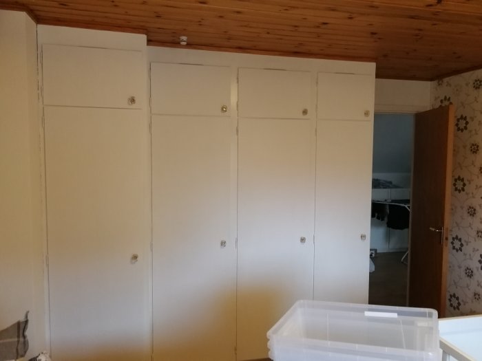 Vit garderob med öppna dörrar i ett rum före renovering.