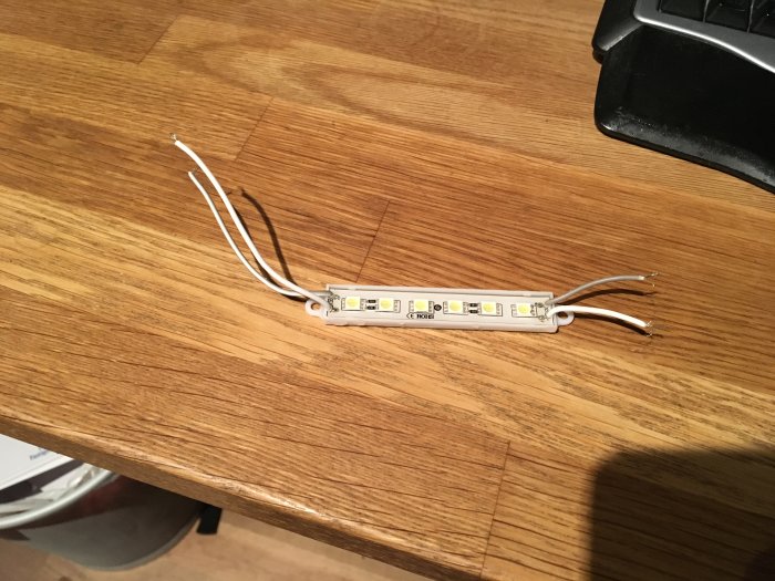 LED-strips med synliga dioder och anslutningskablar mot en träyta.