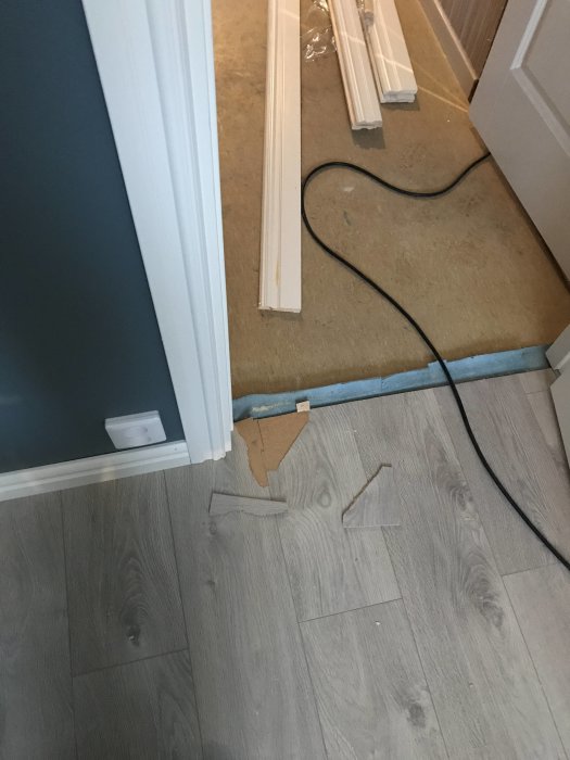 Trasigt golv och dörrfoder med verktyg och golvlister utspridda, efter olycka vid renovering.