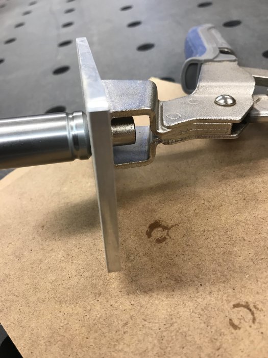 Metallklämma spänd mot ett platt metallstycke på arbetsbord, möjlig deformation vid spänning.