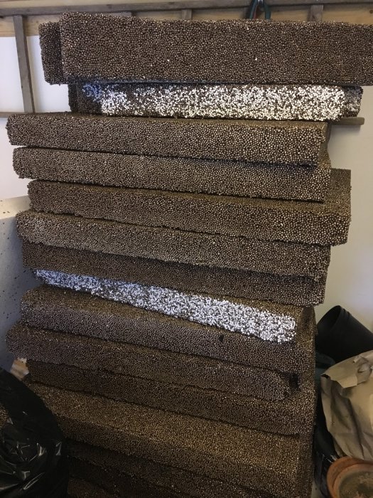 Stapel med bruna isodränskivor, vissa med synligt vita isoleringsdelar, för byggprojekt, några skivor delade.