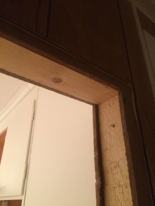 Detaljbild av en vägghörna med synlig träregel och brunt träpanel ovanför, intill en vit gipsvägg.