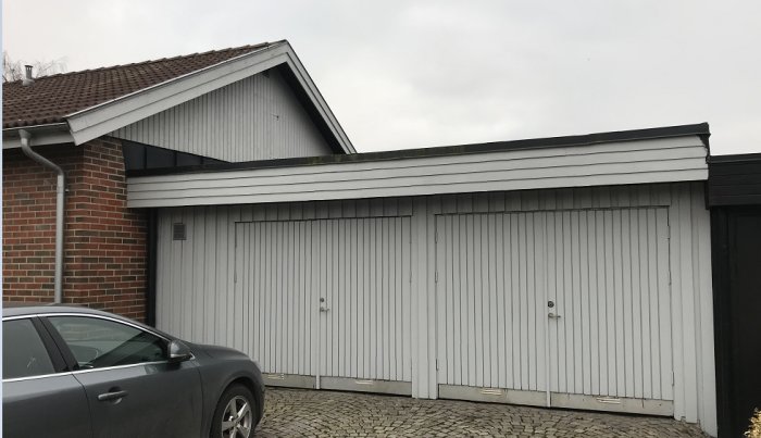 Garage med platt tak intill en tegelhusdel, parkerad bil framför, potentiell renoveringsscen.