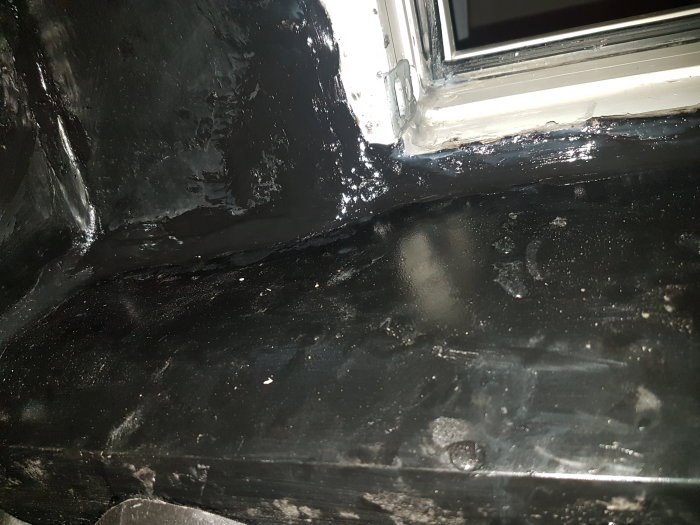 Närbild på tätad fönsterkarm med silikon och synliga vattendroppar på svart plasttäckning.