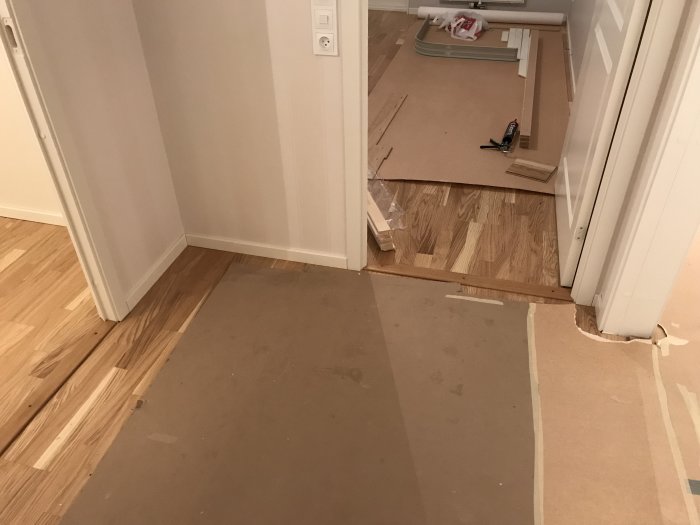 Golvlister och en del kapade trästycken på ett skyddspappbelagt parkettgolv under renovering.