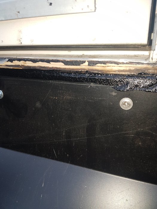 Närbild på en fönsterkarm med synliga skador och tätklister, och tecken på fukt vid en regel bakom pappen.