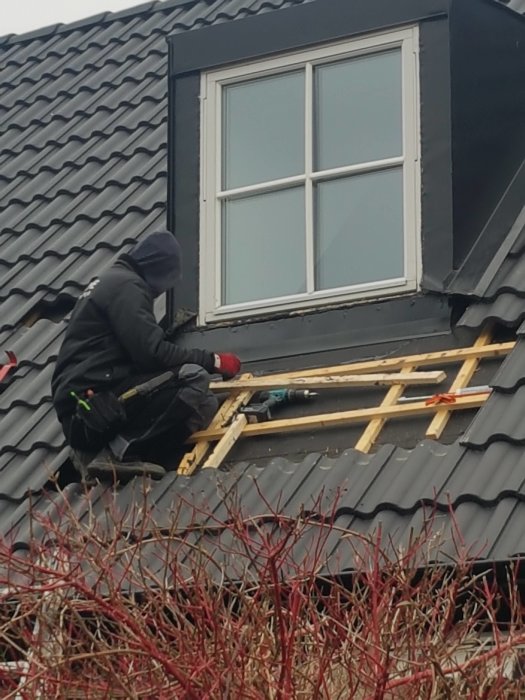 Person reparerar fönsterkarm på ett tak, med synlig vattenskada och skyddspapper runt konstruktionen.