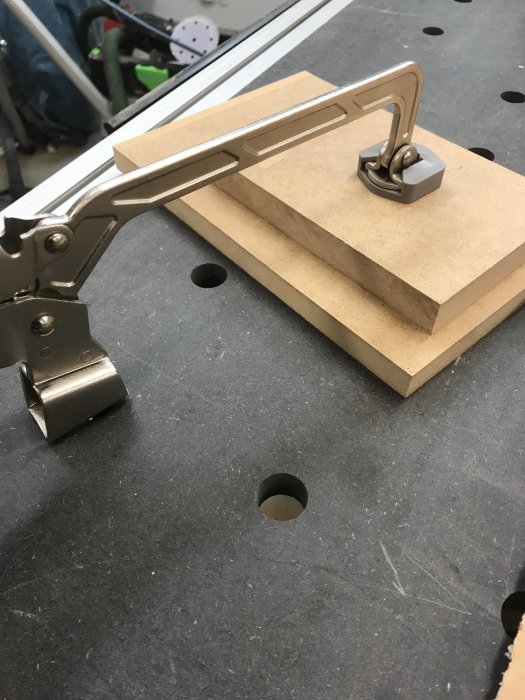Metallklämma fäst på en 19 mm MDF-skiva som visar deformation på arbetsbänk med hål.