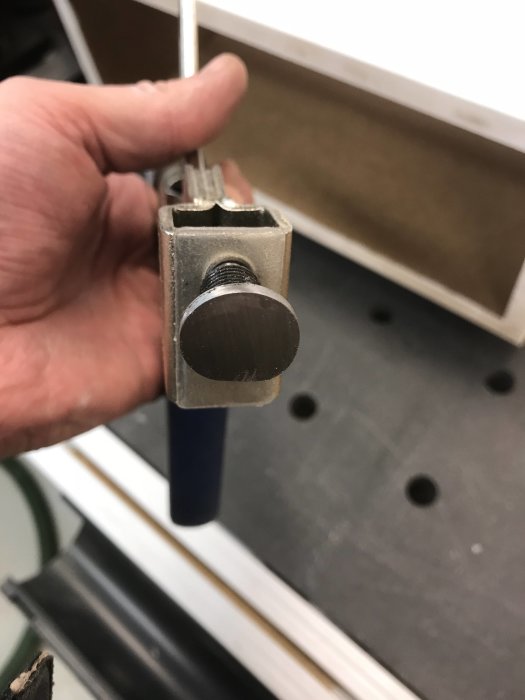 Närbild av en hand som håller en MA-Dog verktygsklämma med en bordskiva i bakgrunden.
