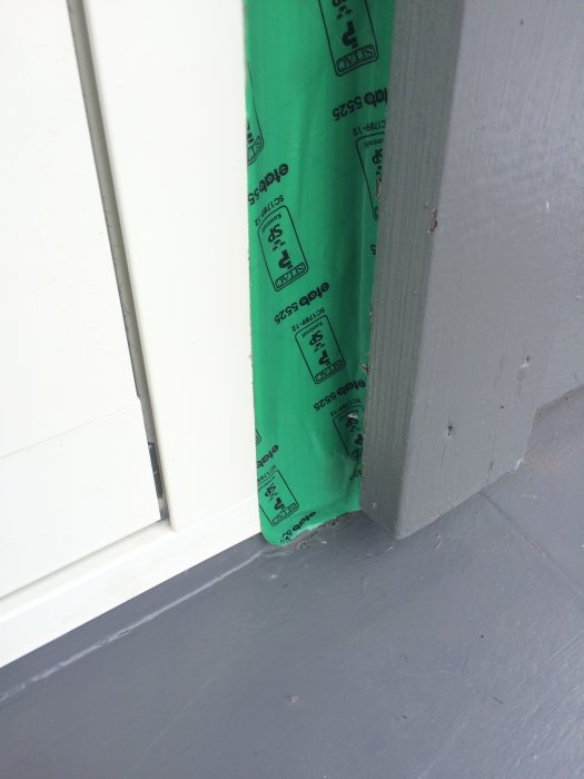 Detaljbild på tätad fönsterinstallation med grön tejp, plåt och silikonering i hörnet av ett hus.