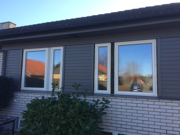 70-talshusfasad med tegel och panel, fönster med fönsterbleck och plåtarbete.