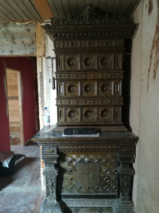 Ornate antique cast iron stove in a room under renovation with exposed walls and ceiling beams.