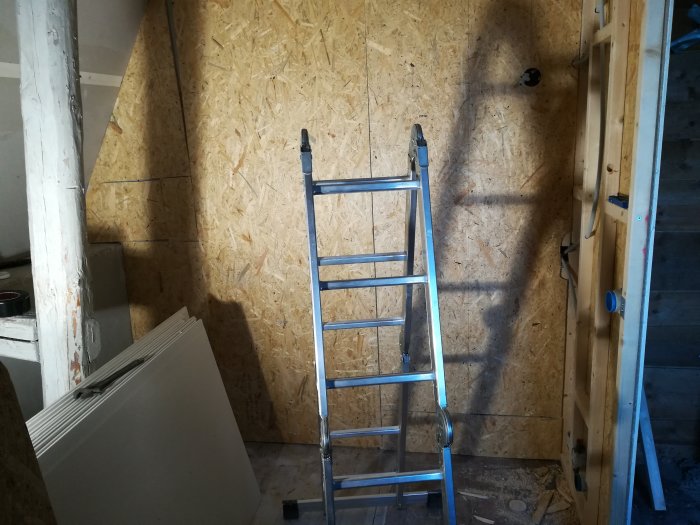 Renoverad garderob under konstruktion med OSB-väggpanel och stålstegar, och paneler på golvet.