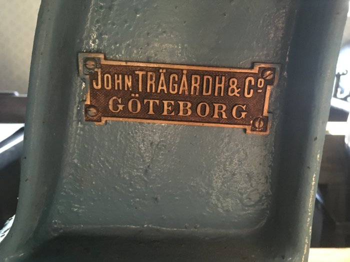 Närbild på en märkplåt med texten "JOHN TRÄGÅRDH & C° GÖTEBORG", en detalj från en handvevad bänkborrmaskin.